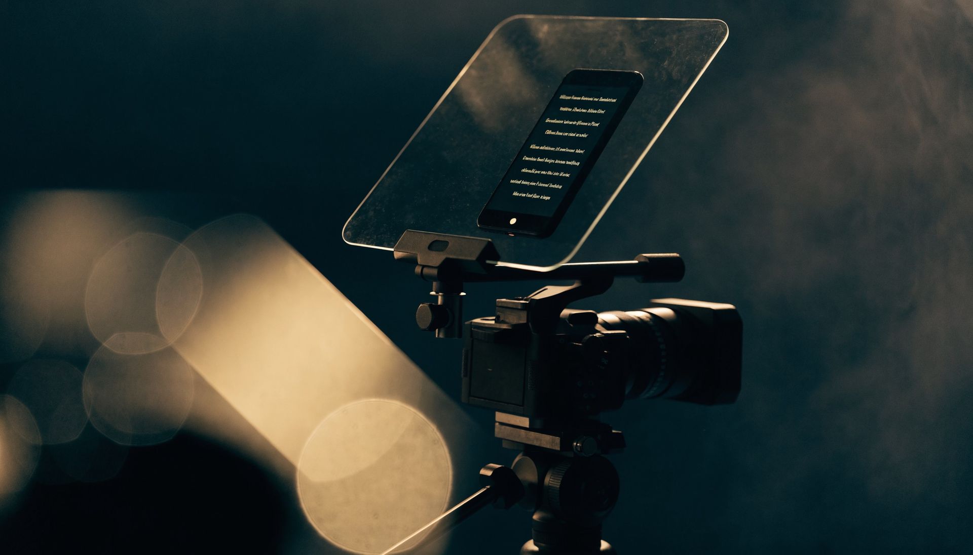 Teleprompter mounted on a camera, phone screen glowing with script text, dramatic gold light — SkyOrbits Oman